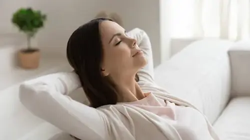 Woman breathing fresh air, feeling happy on the couch in her home.