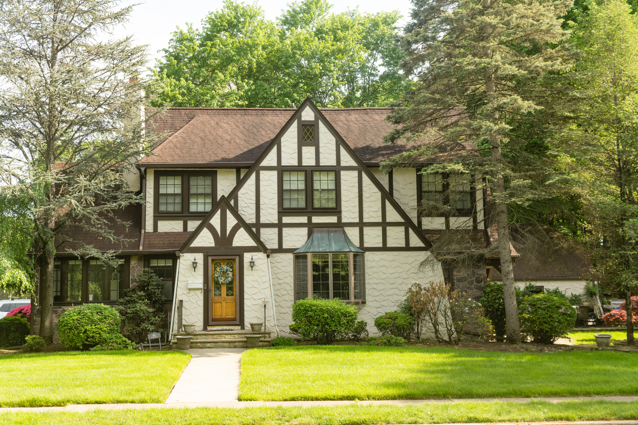 A large European-style residential home sits back from the neighborhood street with a maintained grass lawn.