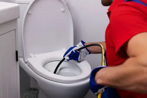 Plumber clearing a clogged toilet with professional drain cleaning equipment.