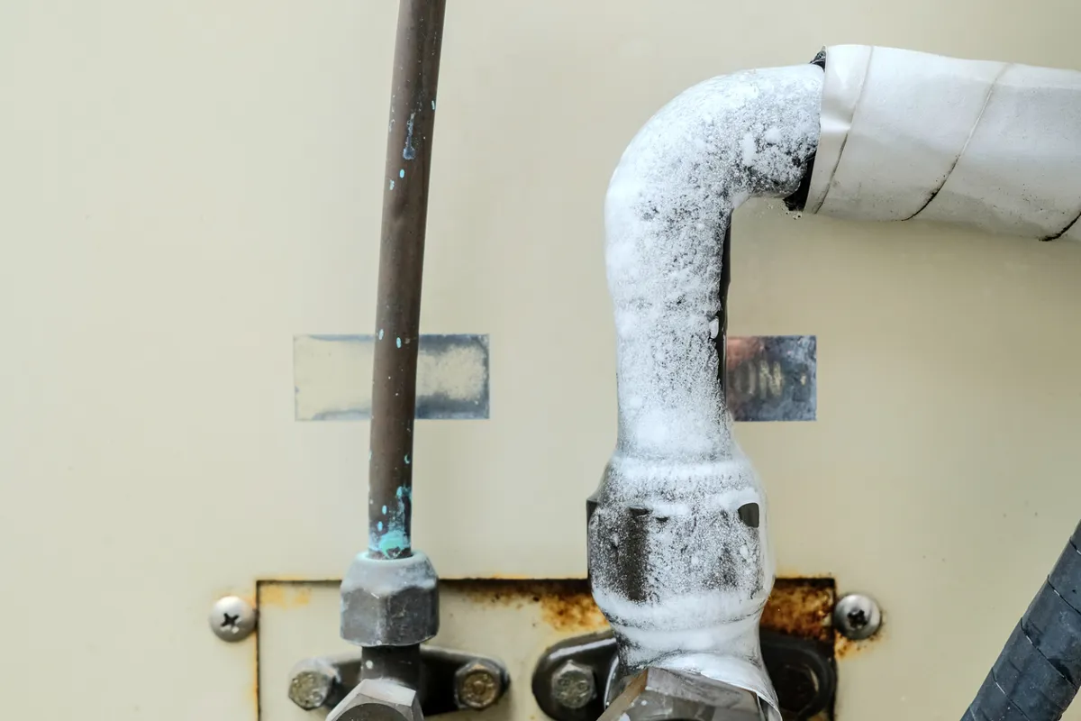 Ice buildup on an air conditioner refrigerant line caused by AC cooling problems.