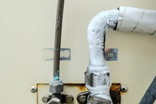 Ice buildup on an air conditioner refrigerant line caused by AC cooling problems.