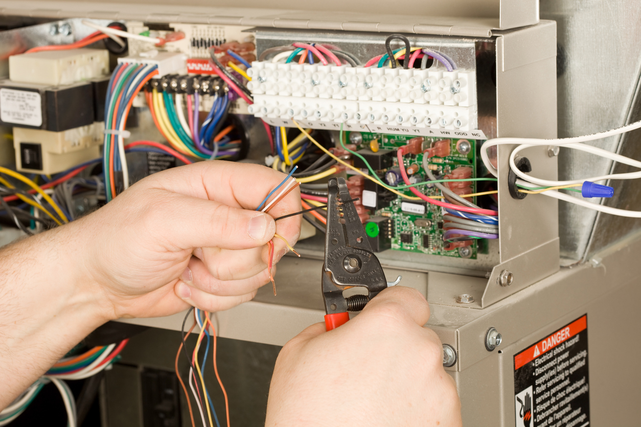 HVAC technician repairing electrical wiring inside a furnace to diagnose a loud or unusual noise.