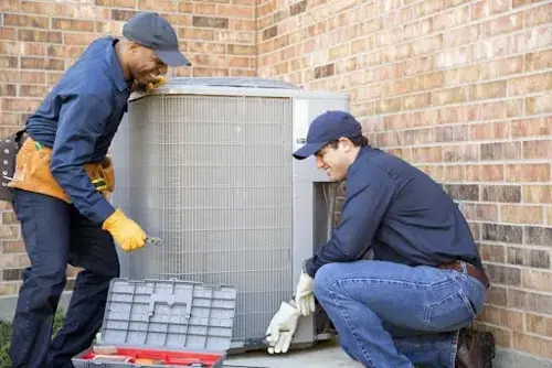 Alt text: HVAC technicians servicing an outdoor air conditioning unit outside a brick home.